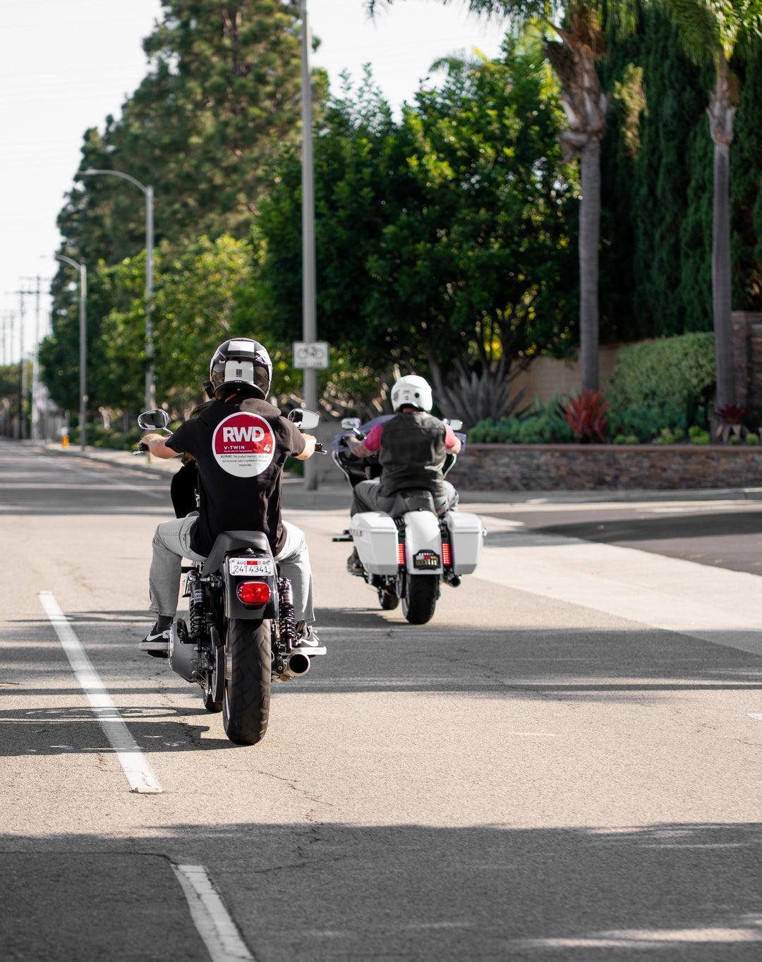 Two Harley Davidson motorcycle riders on a road with the camera at their backs while wearing RWD V-Twin apparel