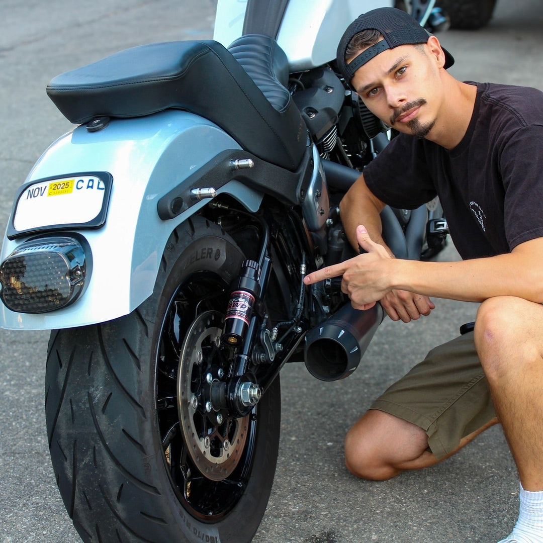 Man kneels next to his Harley Davidson motorcycle and points to his RWD V-Twin rear suspension