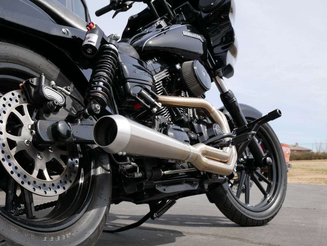 A Harley Davidson motorcycle sits parked on a road with the rear shock in sharp focus