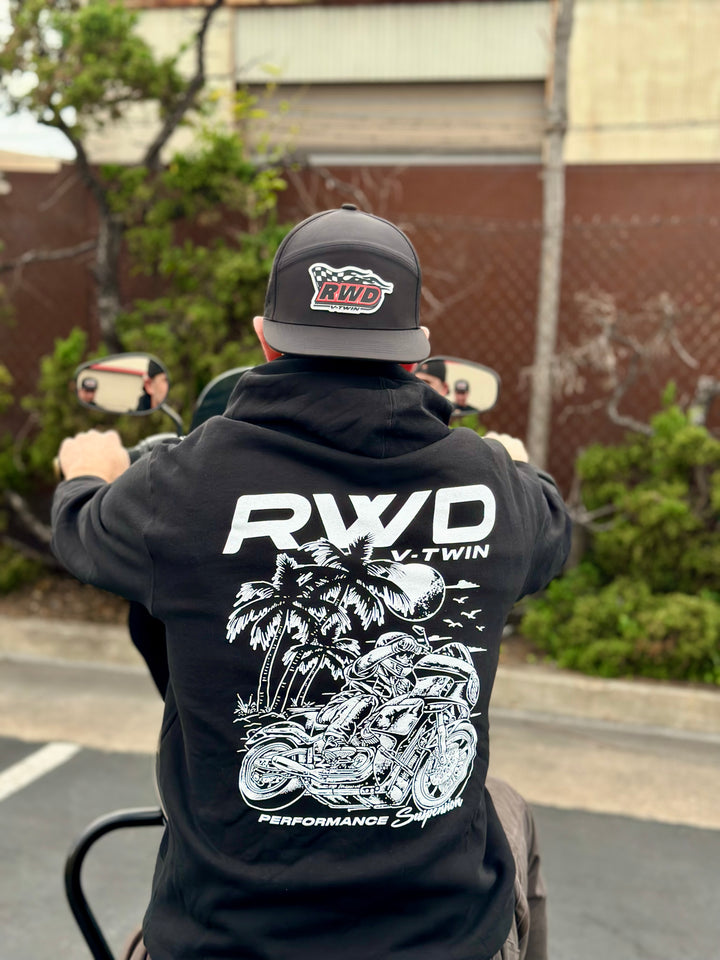 Man sitting on his Harley Davidson in a parking lot while wearing an RWD hat and hoodie